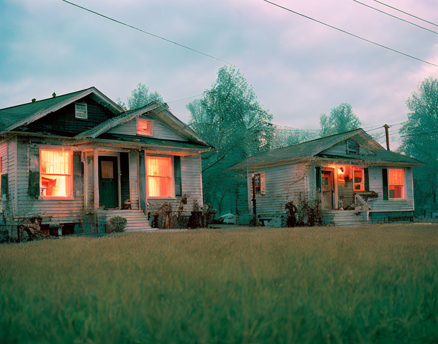 Weathered wooden houses at twilight with warm glowing light and lush green surroundings