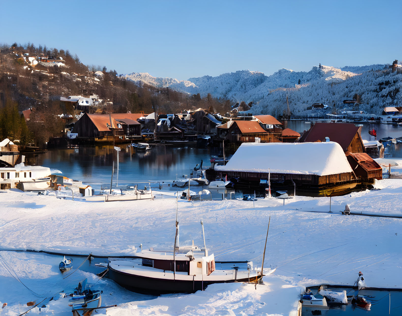 Winter scene: frozen lake, boats, traditional houses, hills, blue sky