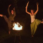 Stylized red-haired women in unique outfits with floating horse heads and a candle