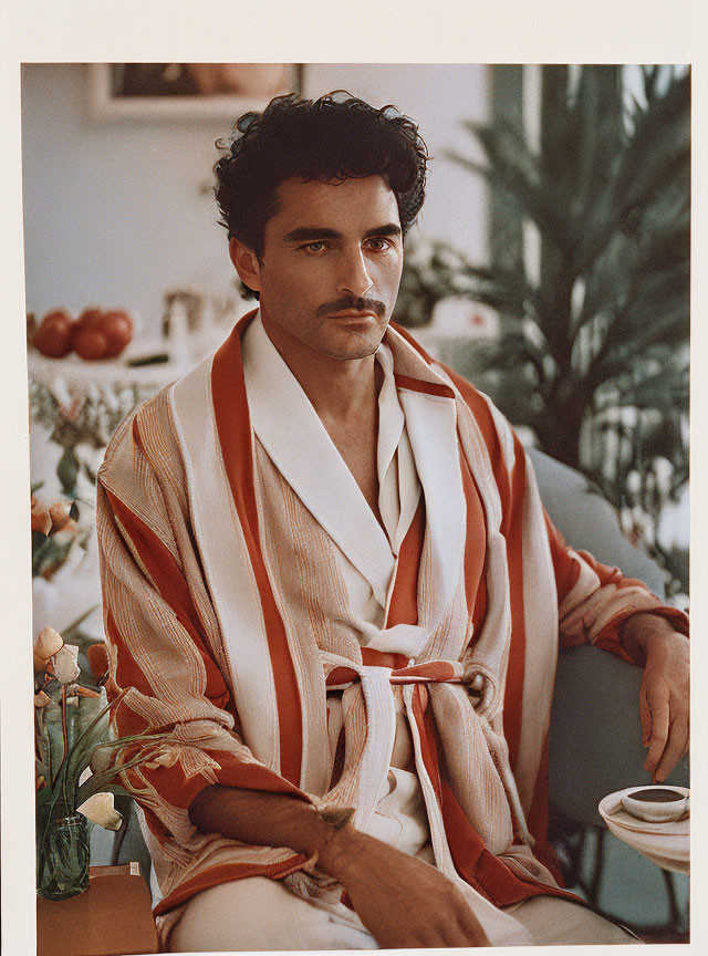 Man in Striped Robe Sitting at Table with Plants and Fruit