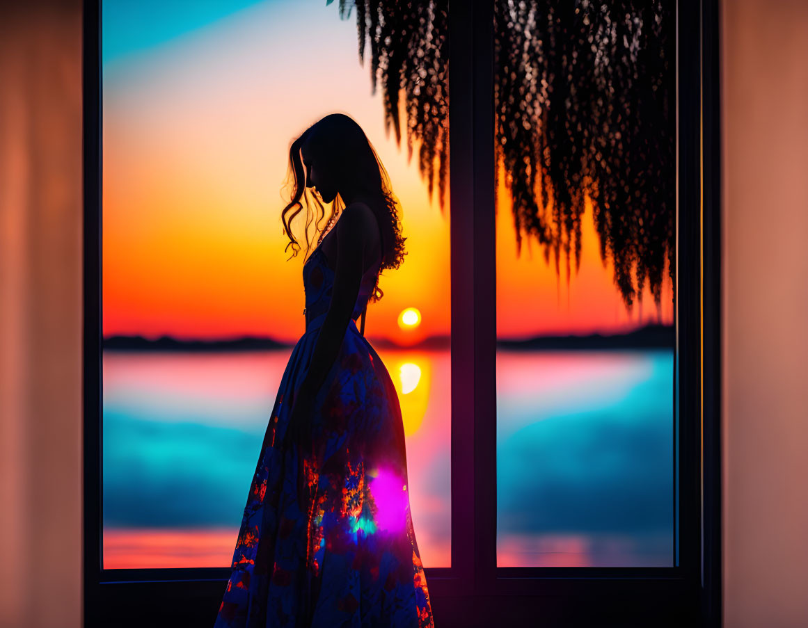 Woman silhouetted at sunset by window overlooking tranquil lake