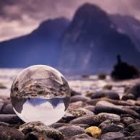 Tranquil island landscape in crystal ball with trees and huts against dark cloudy sky