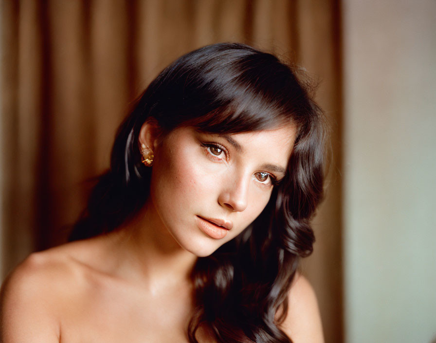 Portrait of woman with brunette hair, soft waves, bare shoulders, gazing at camera