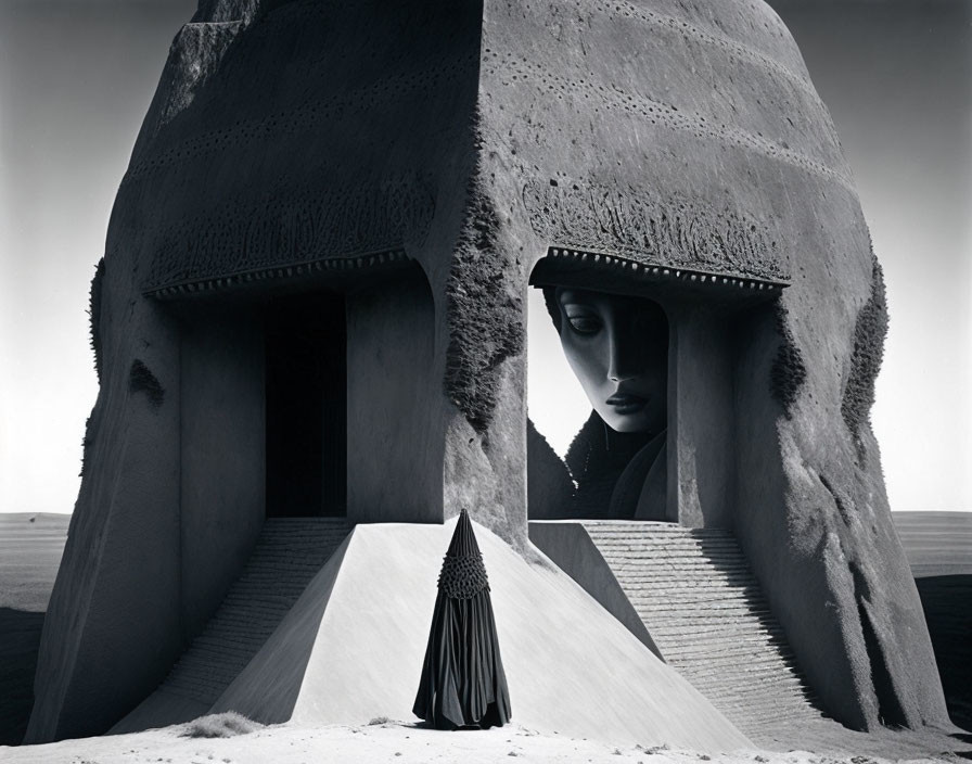 Monochrome surreal image of person in cloak by giant head sculpture