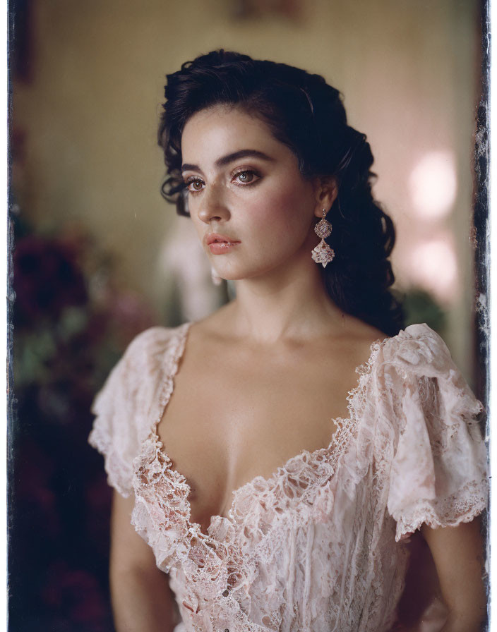 Dark-haired woman in vintage lace dress and earrings gazes intently with blurred floral background