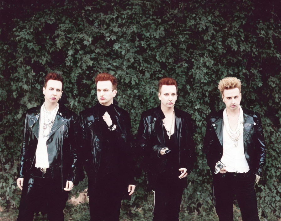 Group of four individuals in punk-inspired outfits and hairstyles against green foliage
