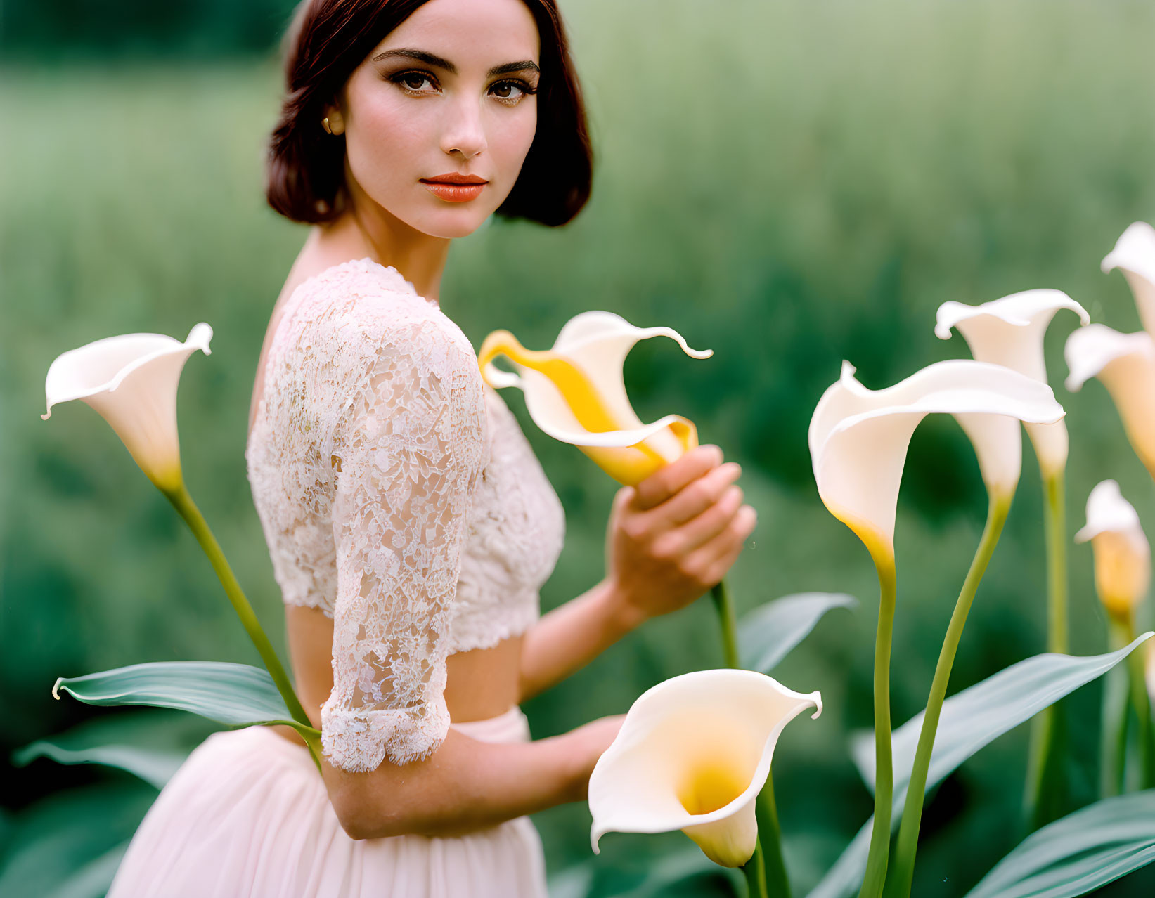 Woman in white lace top surrounded by calla lilies in field