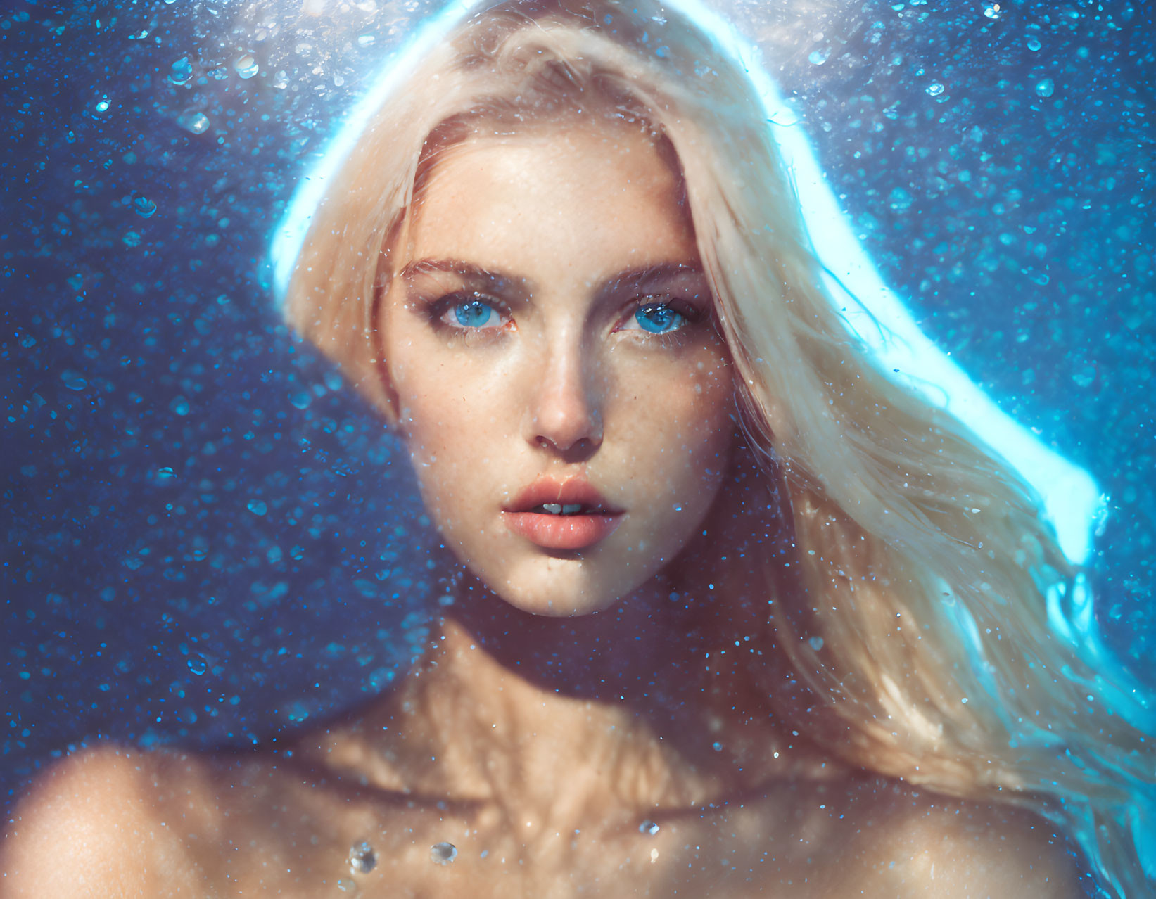 Portrait of woman with platinum blonde hair and blue eyes in water droplets.