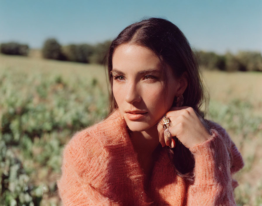 Woman in Coral Sweater Posing in Sunny Field with Large Ring