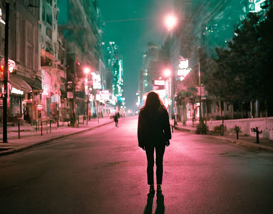 Woman standing in urban street at night with glowing street lights