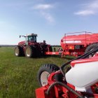 Colorful illustration of blue tractor, red combine harvester, cows, and red plants in green field