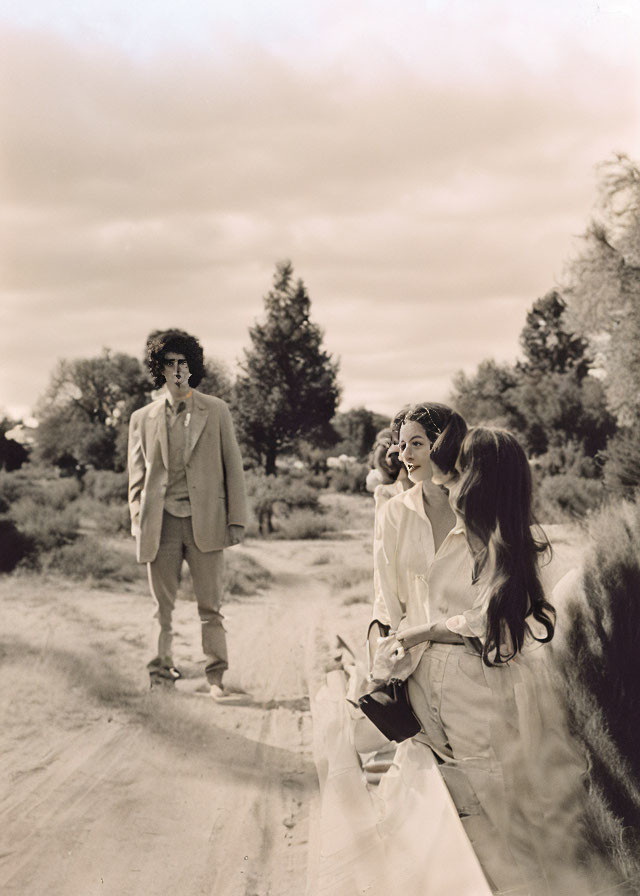 Sepia-Toned Image of Man and Women in Dresses Outdoors