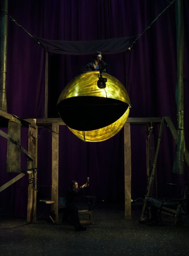 Person performing inside golden sphere with onlooker against purple curtains