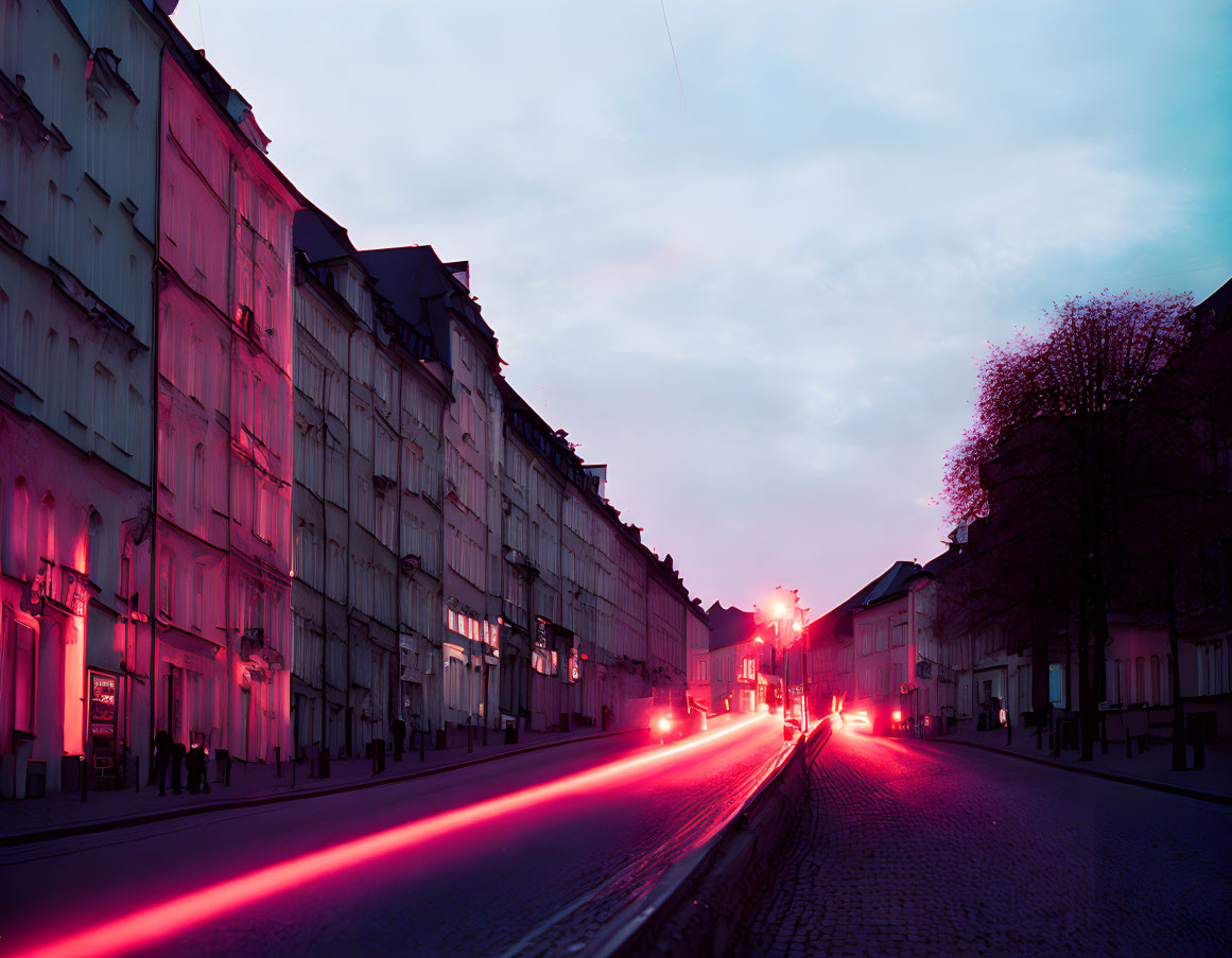 City street at dusk: Pink and blue illuminated buildings, red tail light trails