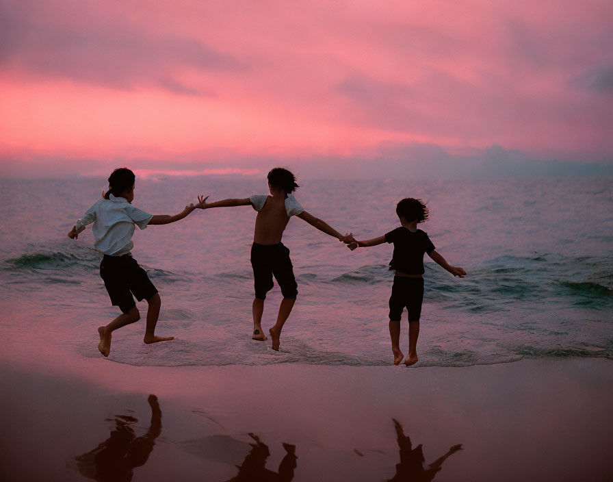 Children playing on beach at sunset with pink skies and calm sea