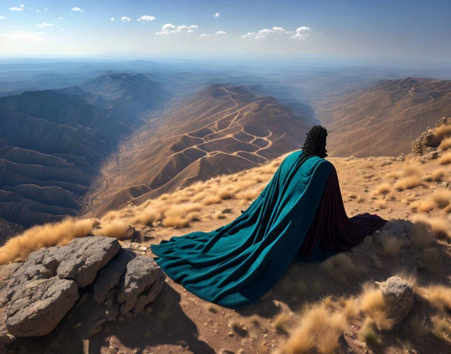 Person in blue cloak gazes at sunlit valley from mountain edge