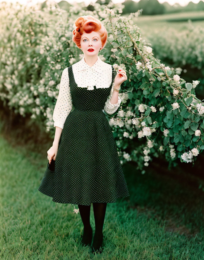 Red-haired woman in updo wearing polka dot dress by flowering bushes