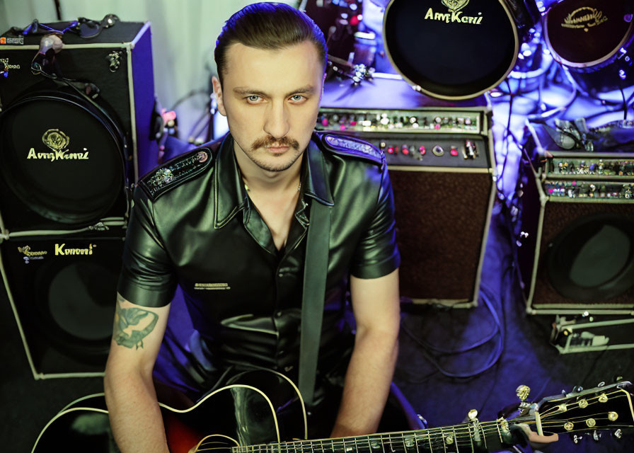 Mustachioed musician in black leather with guitar and amplifiers