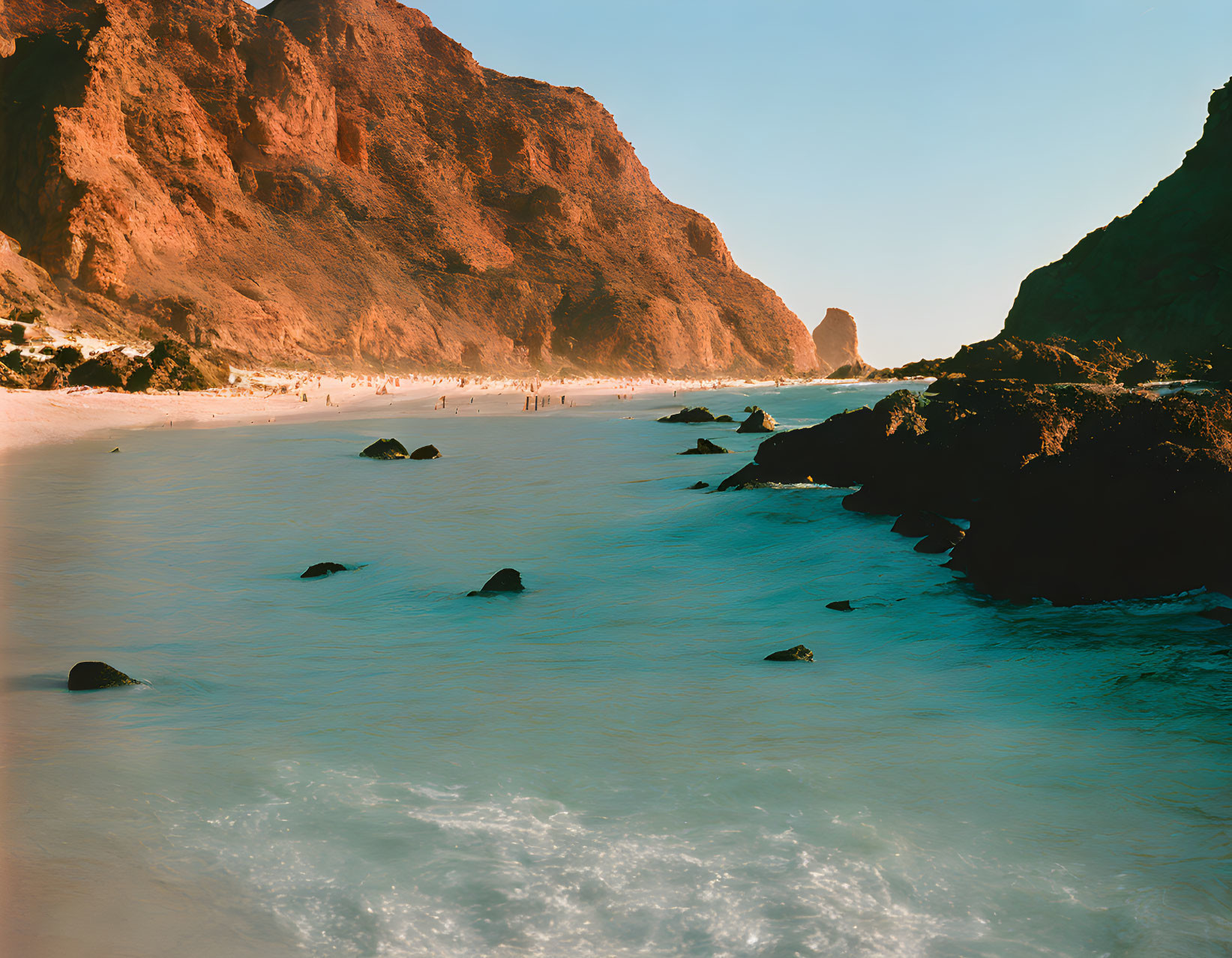 Tranquil beach scene with rocky cliffs and distant figures