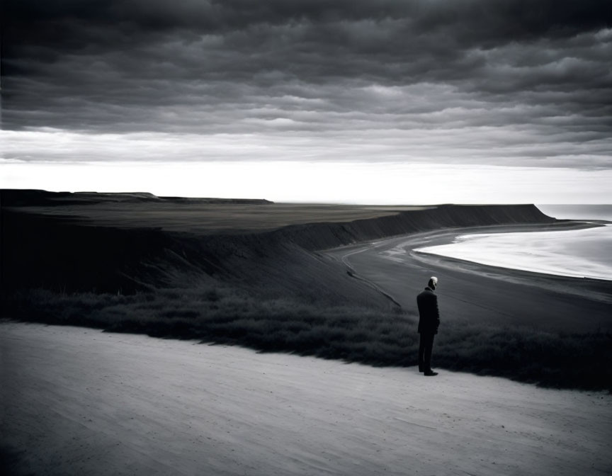 Solitary figure on empty beach with sand dunes under cloudy sky