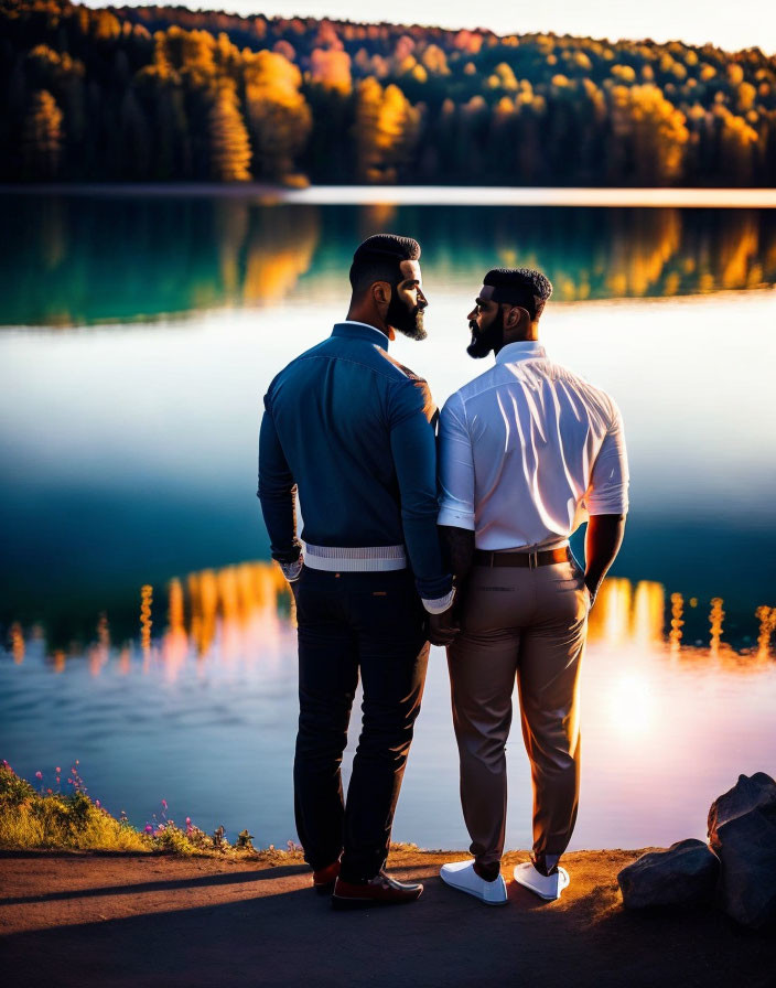 Men holding hands by serene lake at sunset with autumn trees reflected