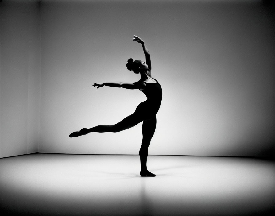 Silhouette of ballet dancer in mid-pose against white backdrop