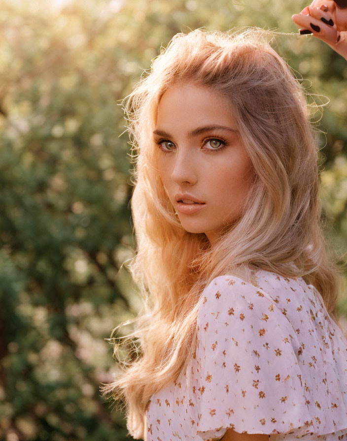 Blonde woman in floral top under sunlight and foliage.