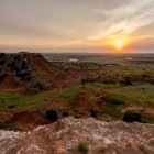 Scenic sunset over mosaic-tiled cliff, river, and green plain