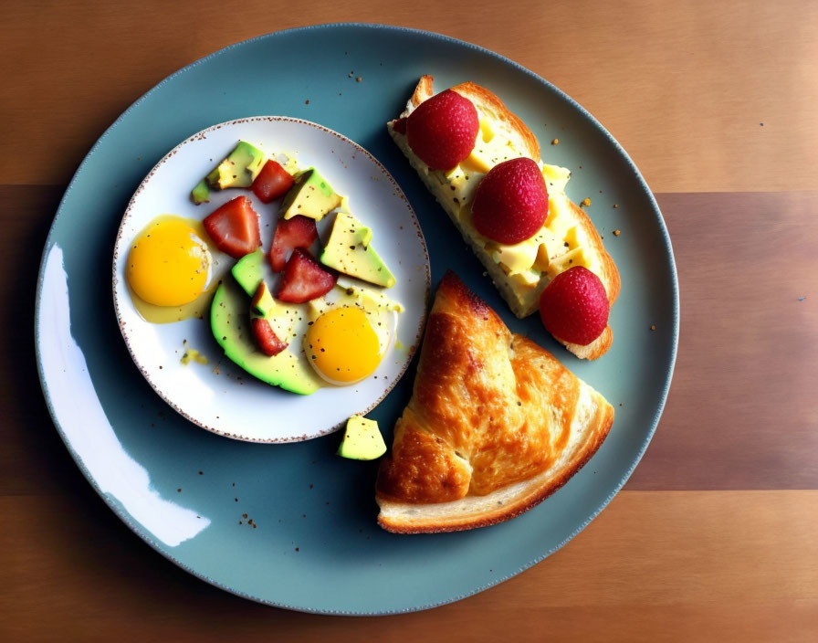 Fresh breakfast plate with avocado, tomatoes, eggs, croissant, toast, cheese, and strawberries on