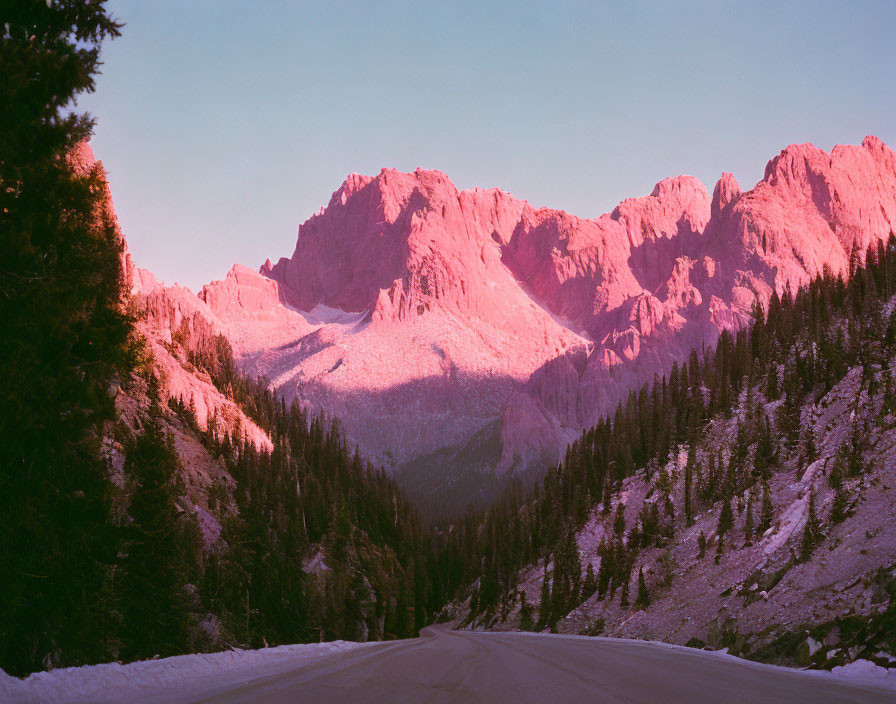 Scenic snowy mountain road at sunrise with pink-hued peaks and forested slopes