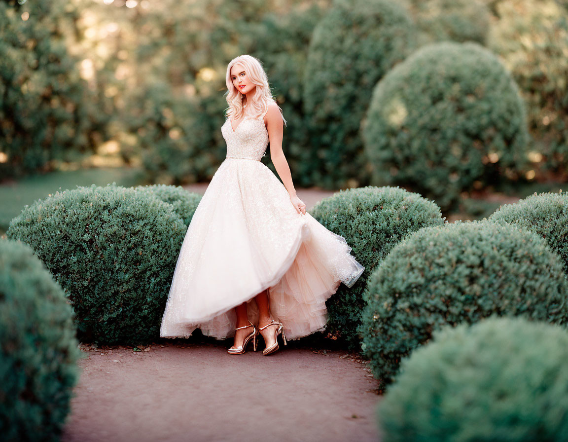 Woman in white gown and golden heels posing in manicured garden setting