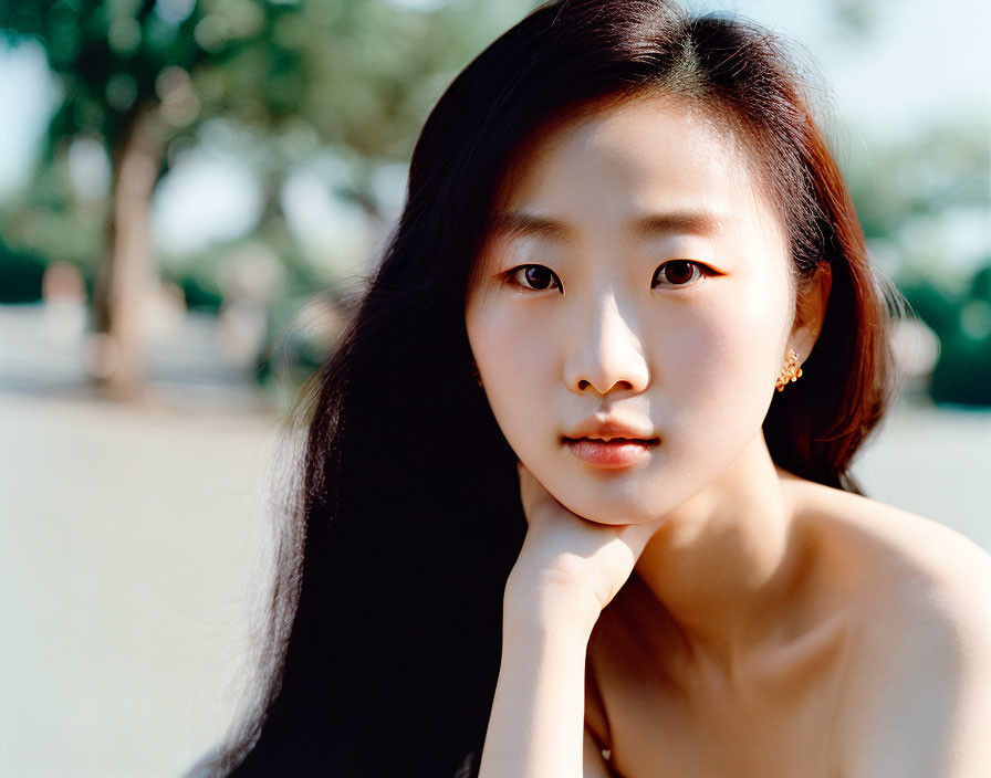 Portrait of young woman with long black hair by trees and water