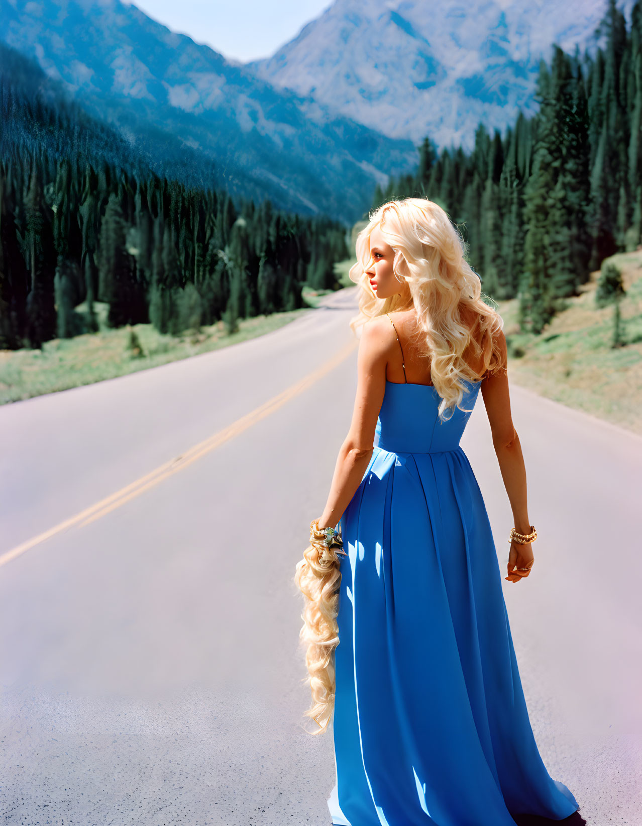 Blonde woman in blue dress on mountain road with pine trees