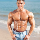 Muscular person with abs and chest on beach in gray shorts and watch