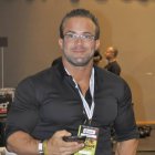 Muscular man with styled hair holding a glass, black shirt, watch, and earring