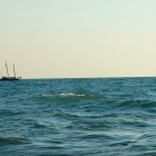 Sailing ship painting on vast ocean with rolling waves under soft cloudy sky