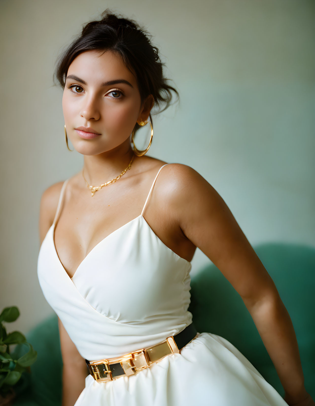 Elegant Woman in White Dress with Gold Belt and Jewelry on Soft Green Background