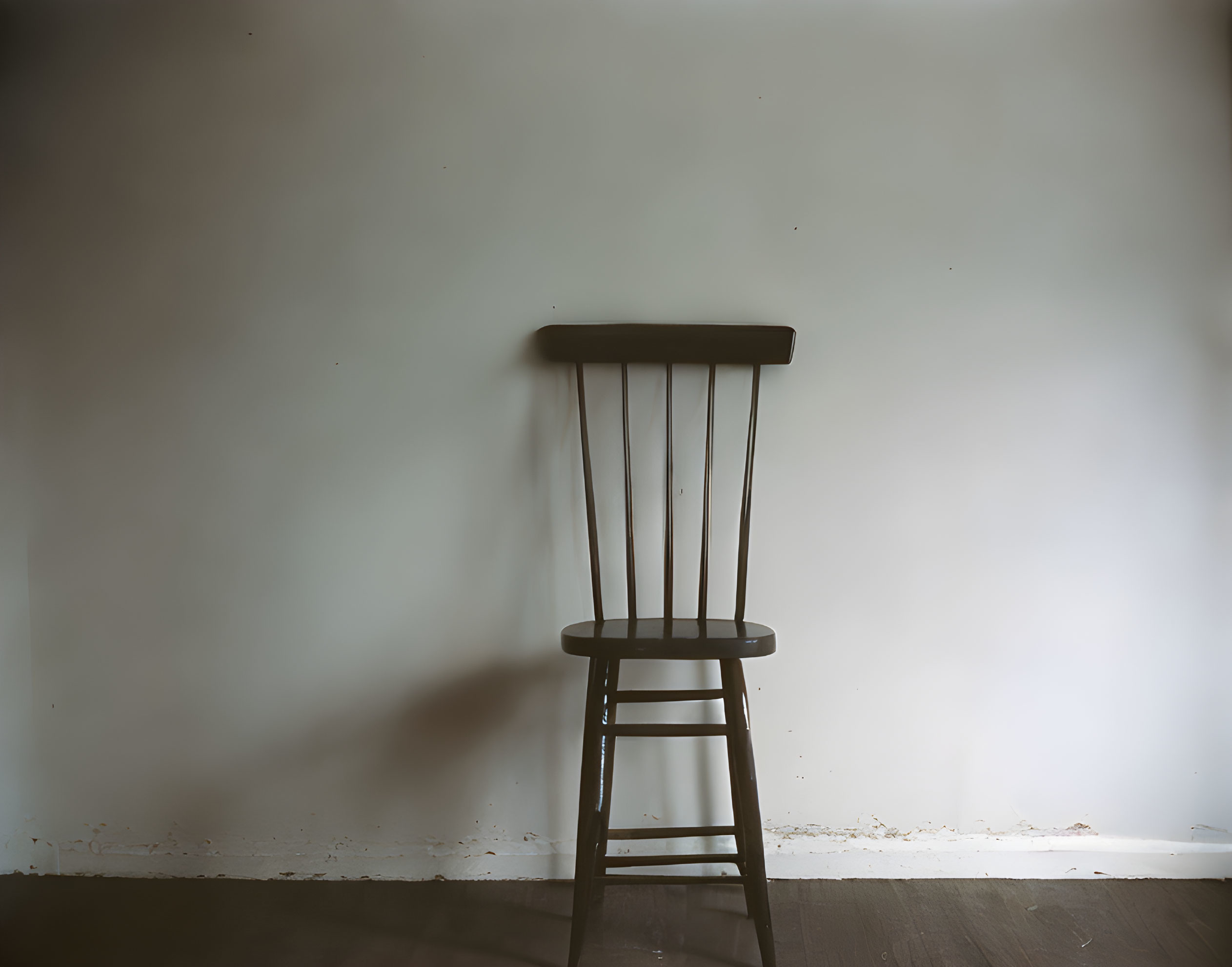 Wooden chair casting shadow against blank wall symbolizes solitude.