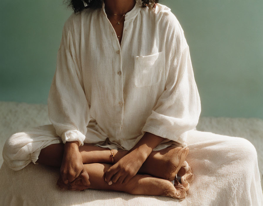 Cross-legged person in white shirt against green background.