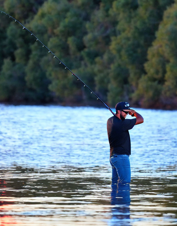 Person in baseball cap fishing in water at dusk