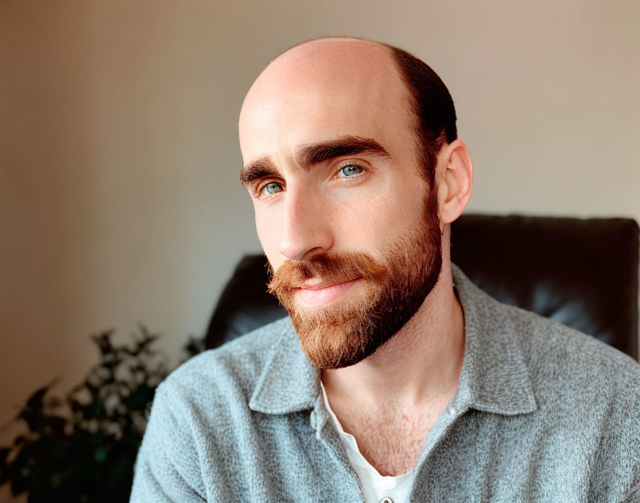 Bald Man with Beard Smiling in Blue Shirt and Plant Background