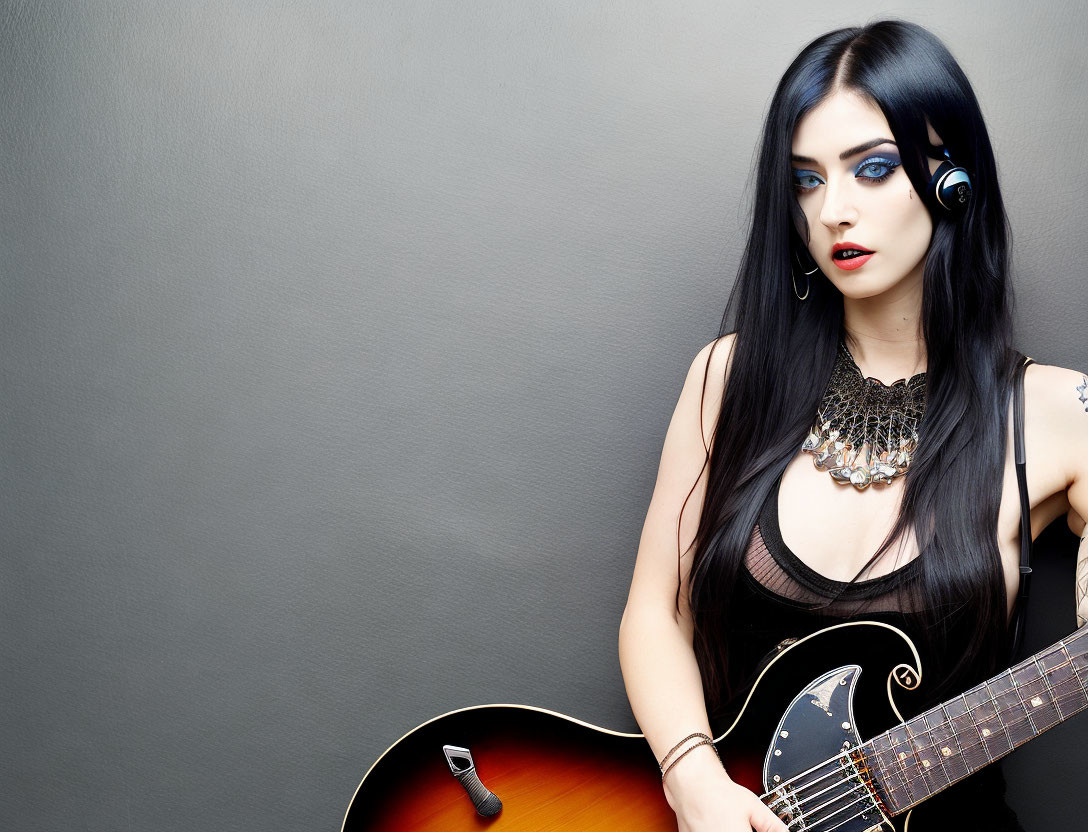 Woman with Black Hair and Blue Eye Makeup Holding Guitar on Grey Background