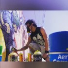 Fashionable individual with braids and sunglasses in colorful attire by graffiti wall with smartphone.