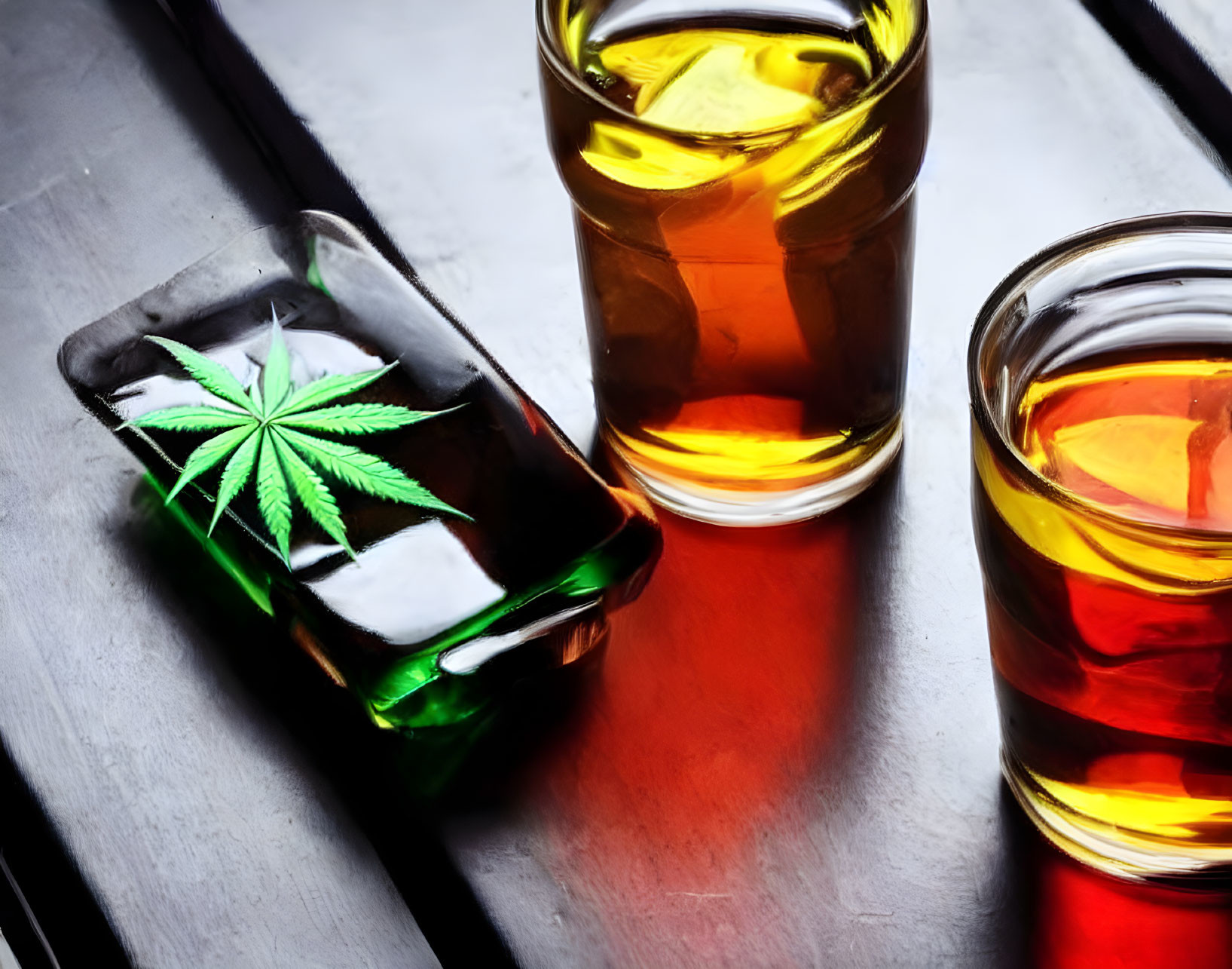 Three glasses of whiskey with ice cubes and a green leaf on reflective surface in moody setting