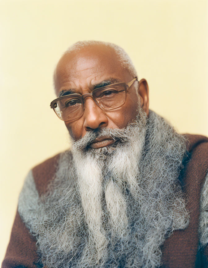 Elderly man with gray beard and glasses on pale yellow background