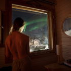 Person in Orange Jacket Gazes at Aurora Borealis from Cabin Window