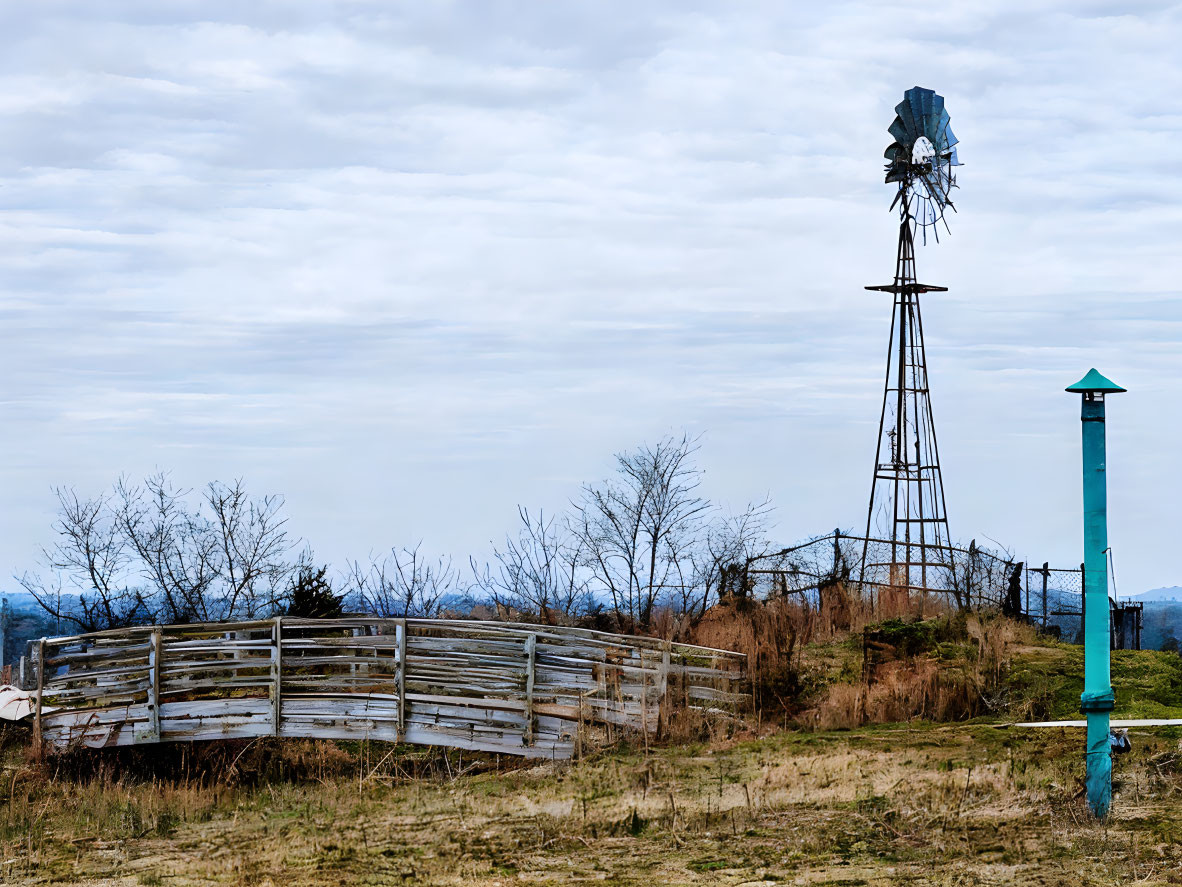 Rusty windmill and wooden corral under cloudy sky in grassy field