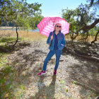 Fashionable person strolling under pink umbrella on flower-lined path