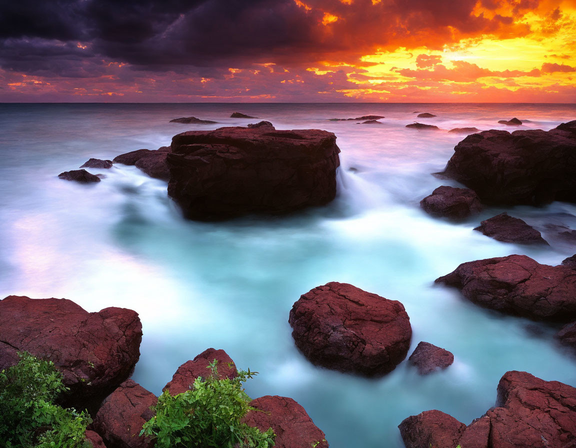 Serene ocean sunset with dark rocks under vibrant sky