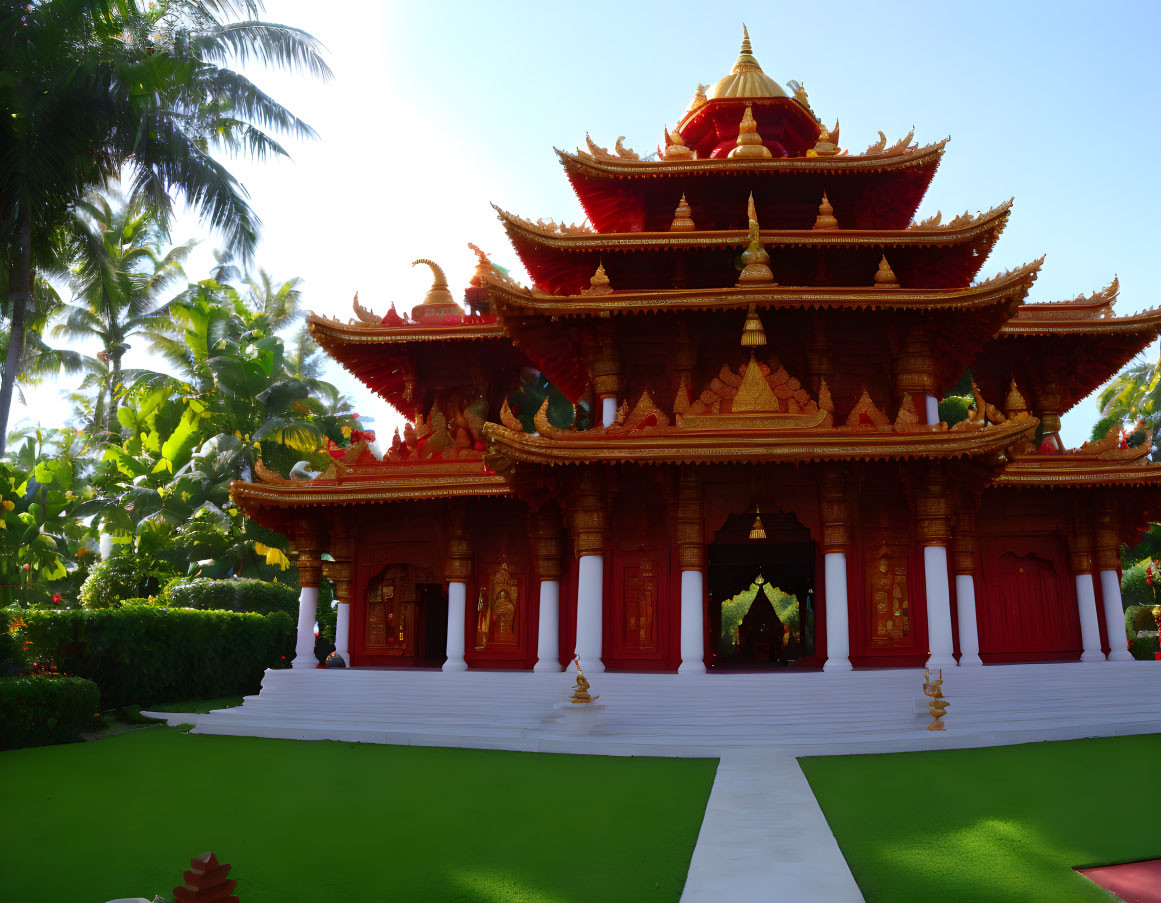 Traditional red and gold pagoda-style temple with multiple tiers in lush greenery against blue sky